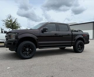 Dark brown Ford F 150 truck with black wheels, tinted windows, and a black roll bar parked outdoors.