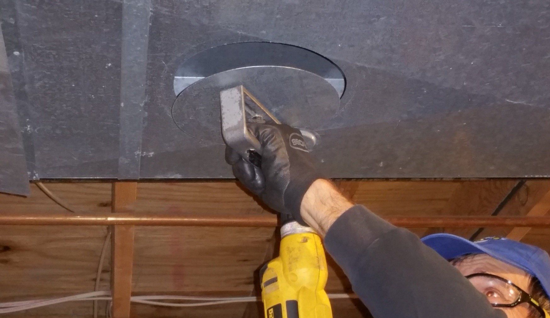 A man is using a hammer to cut a hole in the ceiling.