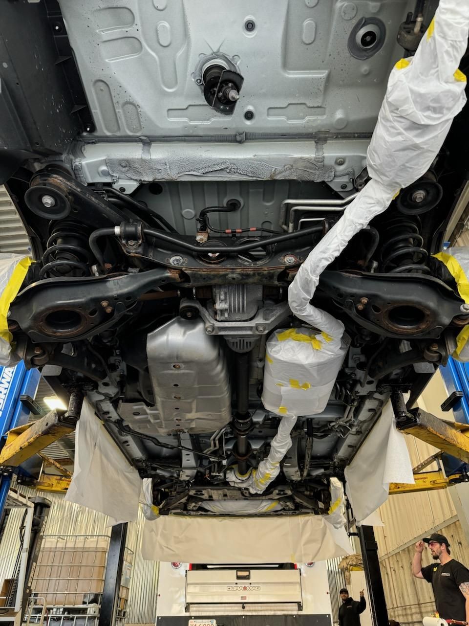 The underside of a car is being worked on in a garage.