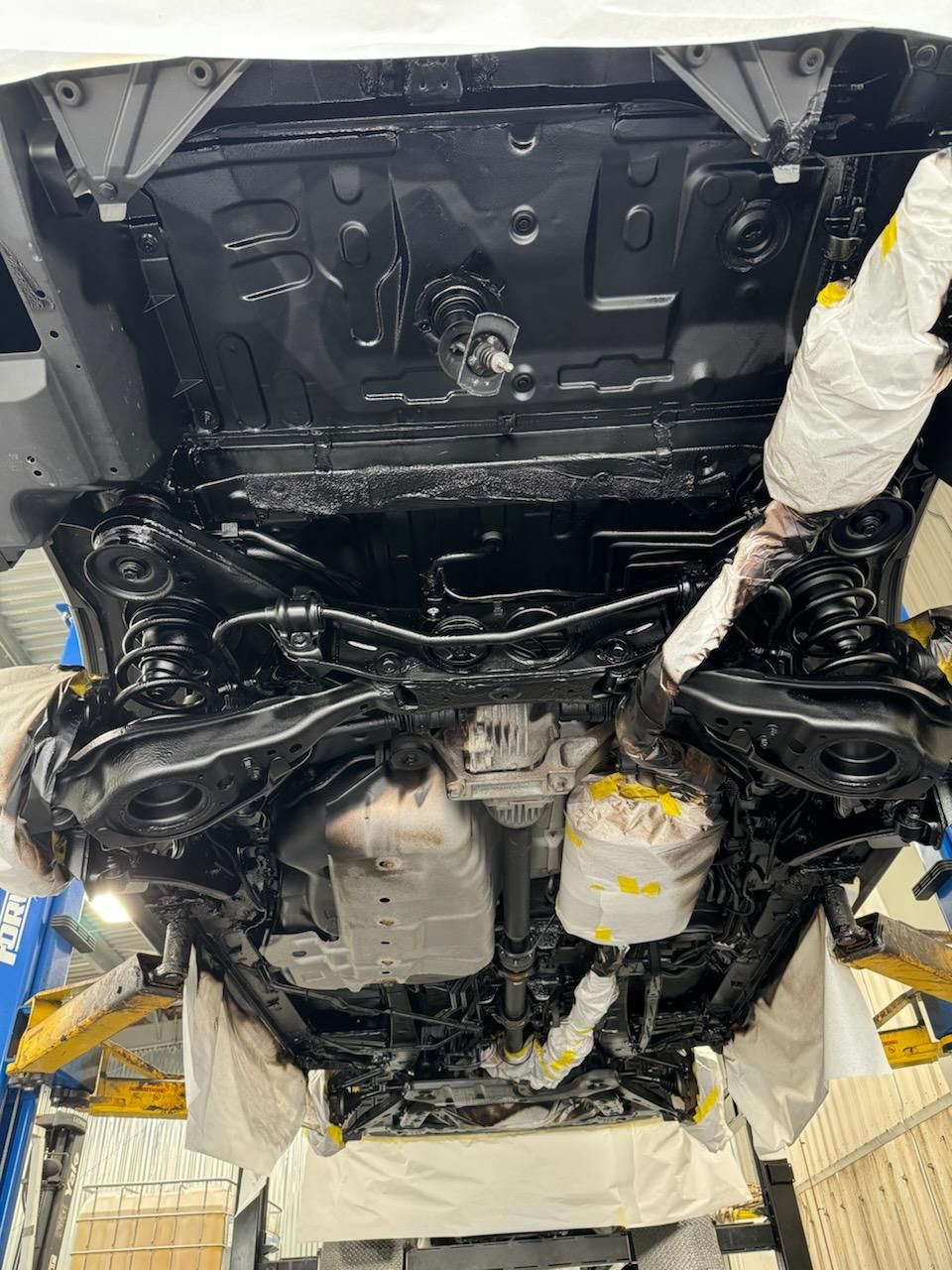 The underside of a car is being painted black.