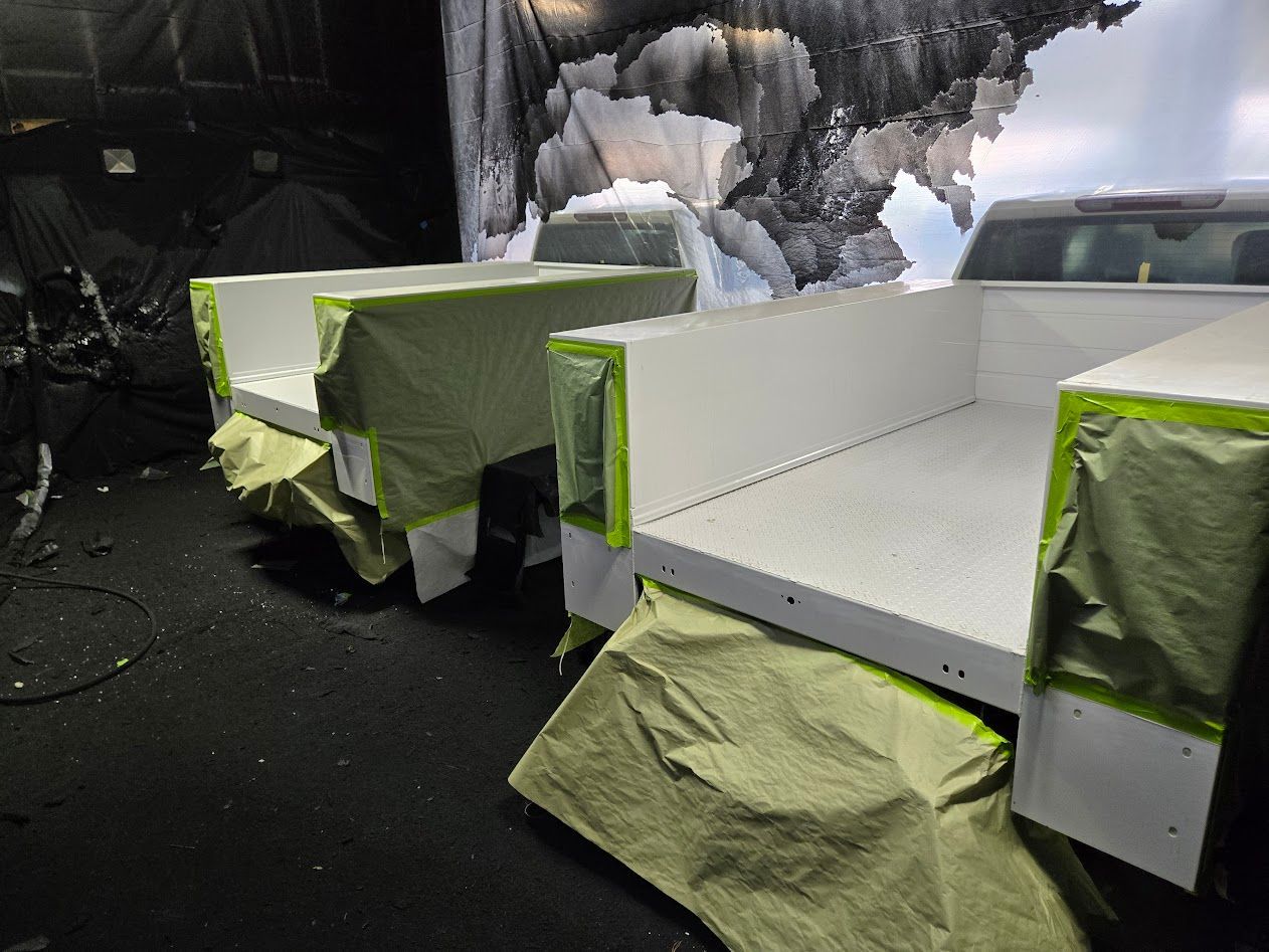 Two white truck beds taped for painting; in a dark setting, with a backdrop.