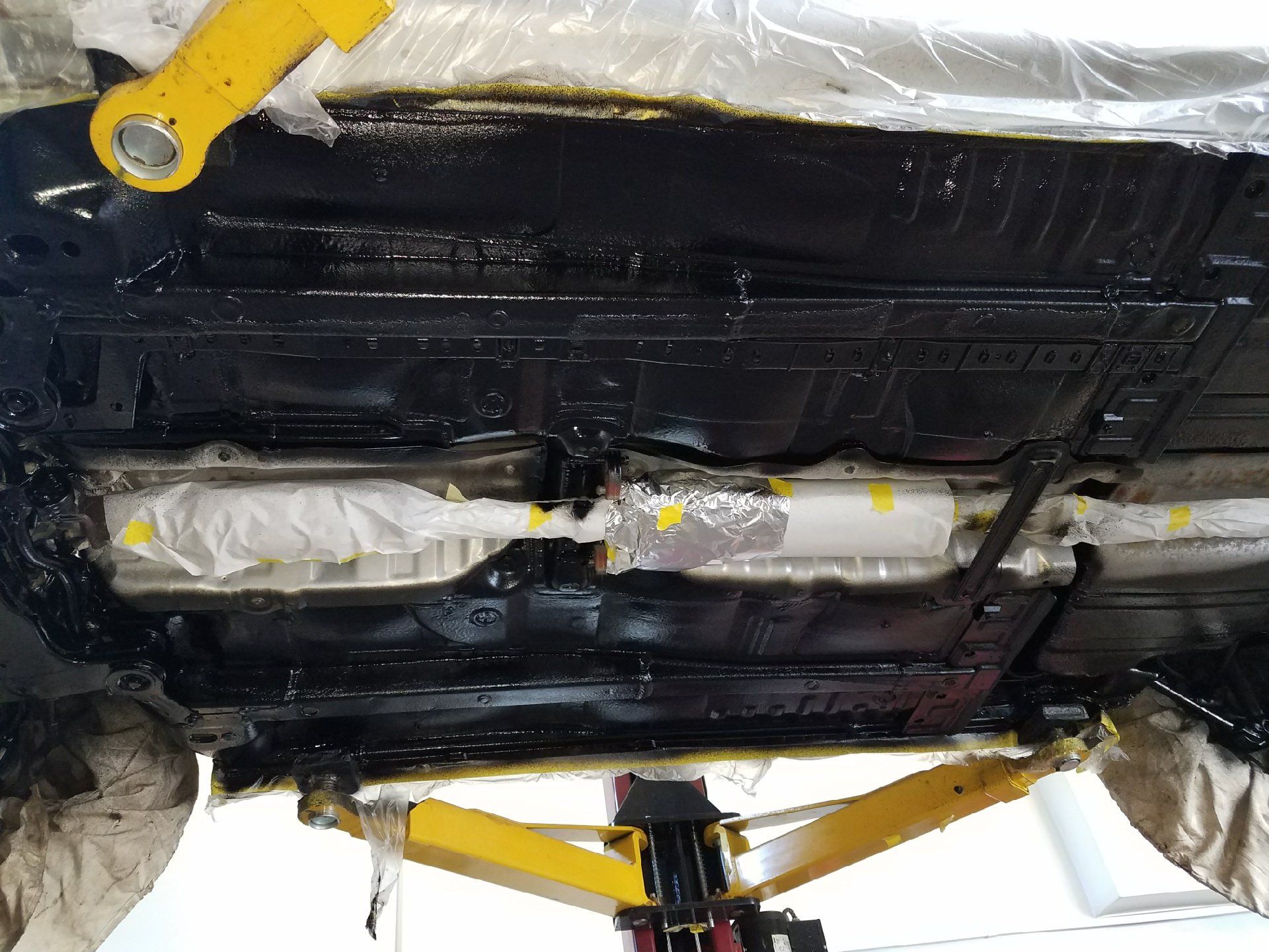 The underside of a car is sitting on a yellow lift.