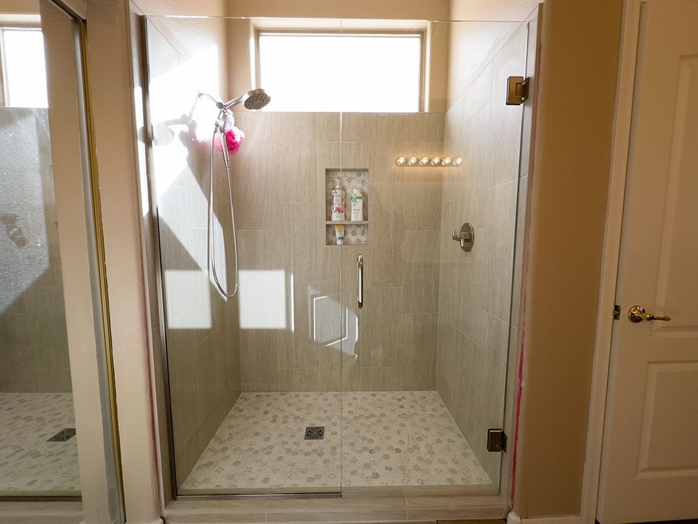 A walk in shower with a glass door and a window.