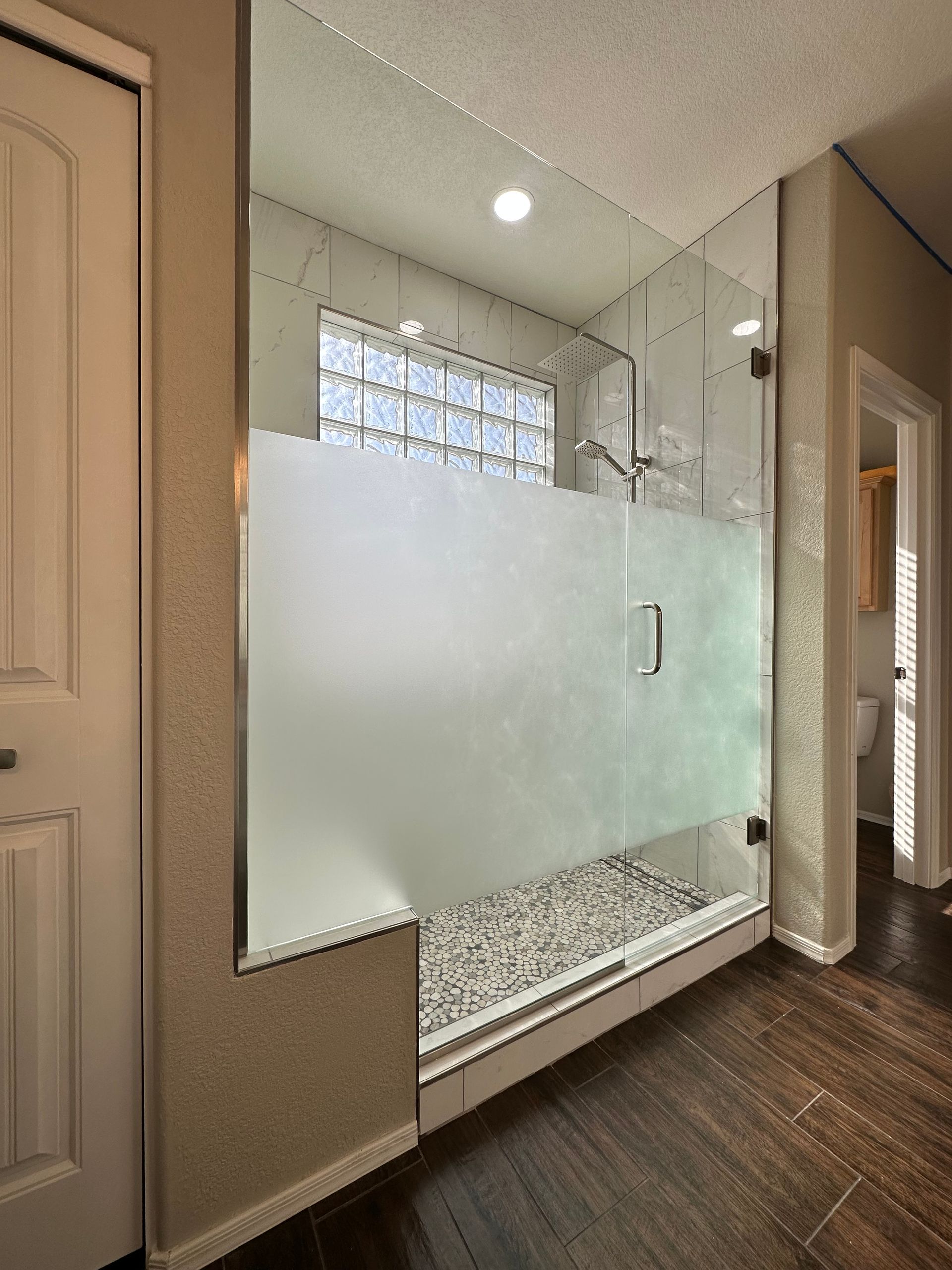 A bathroom with a walk in shower with a frosted glass door.