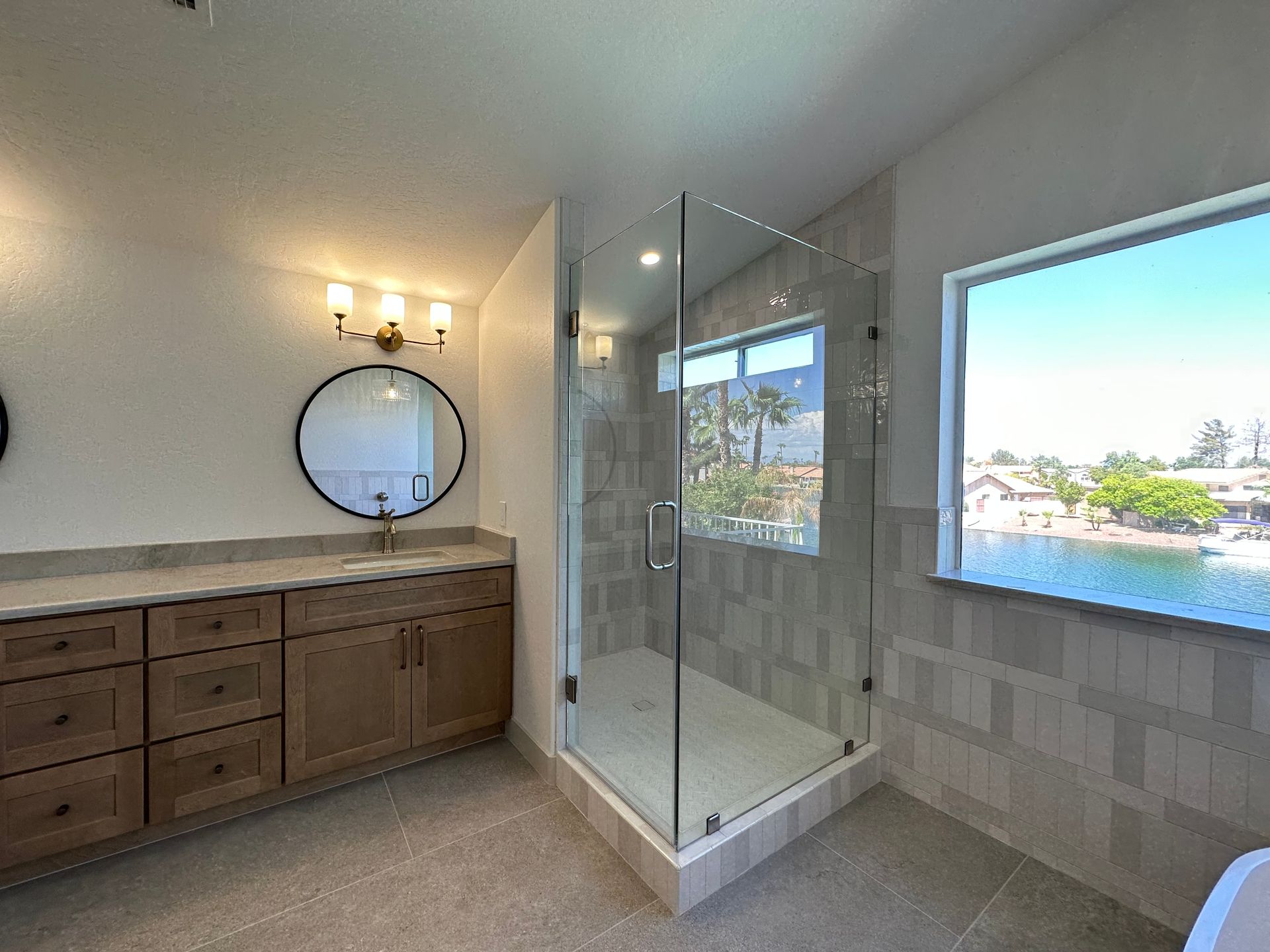 A bathroom with a walk in shower, sink, mirror and window.