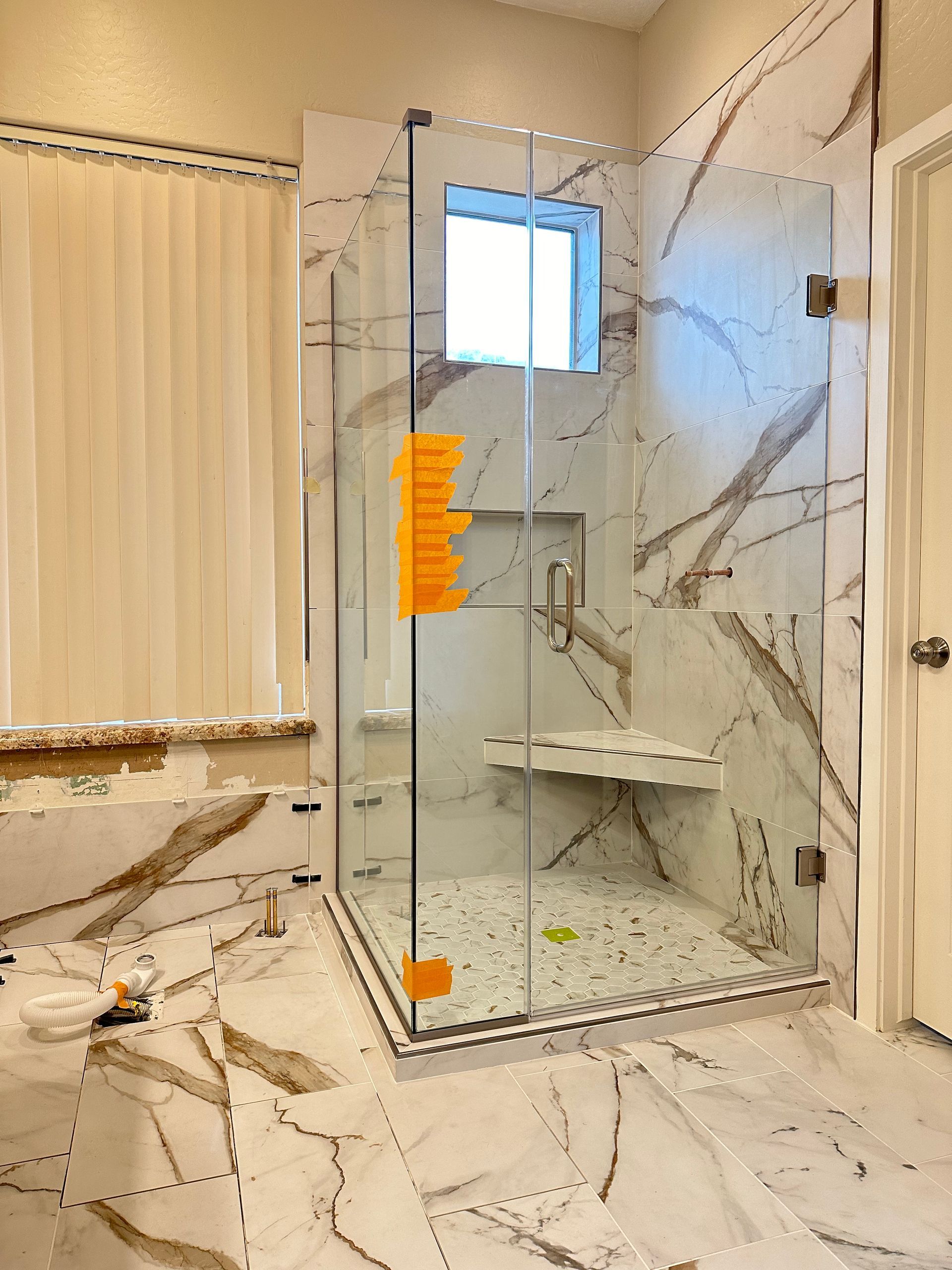 A bathroom with marble tiles and a walk in shower with a glass door.