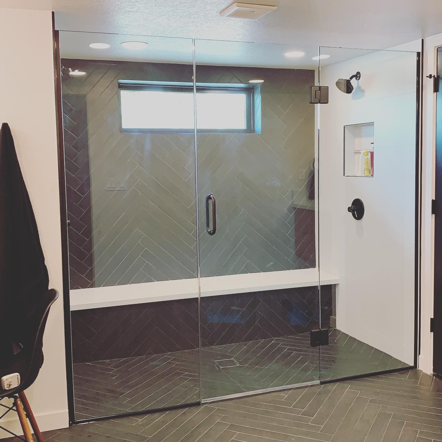 A bathroom with a glass shower door and a bench