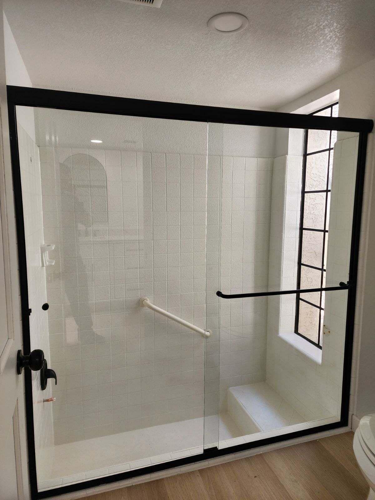 A bathroom with a sliding glass shower door and a window.