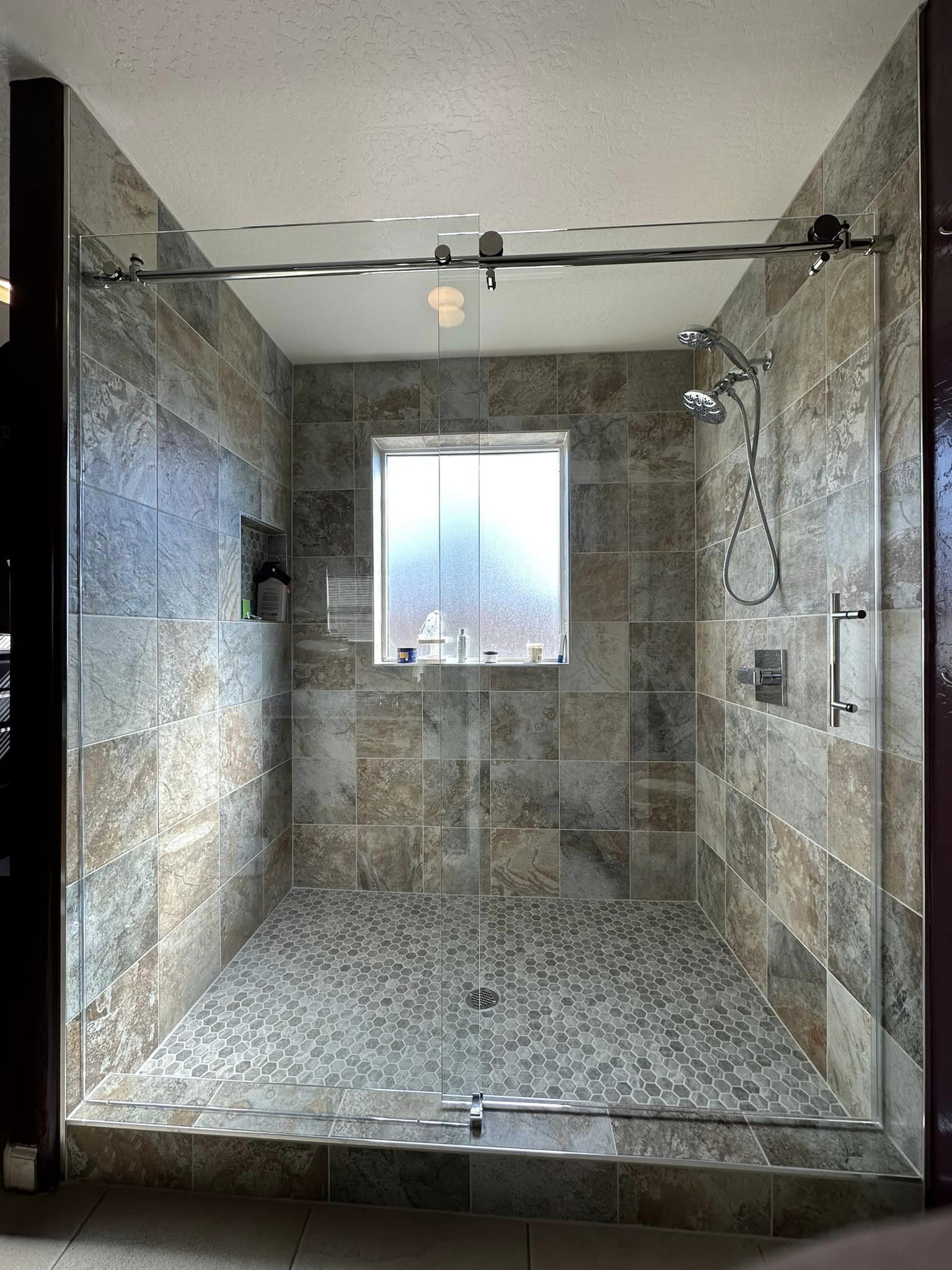 A walk in shower with a sliding glass door and a window.