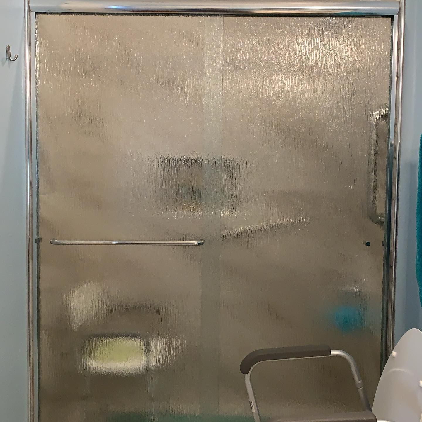 A shower door with a stainless steel frame and handles in a bathroom.