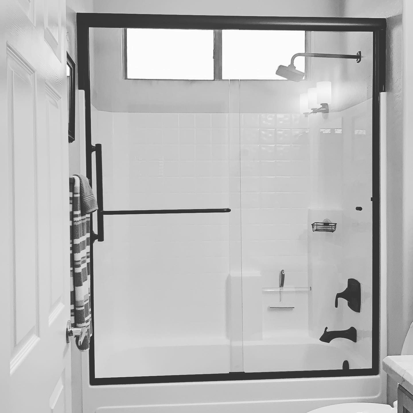 A black and white photo of a bathroom with a sliding glass shower door.