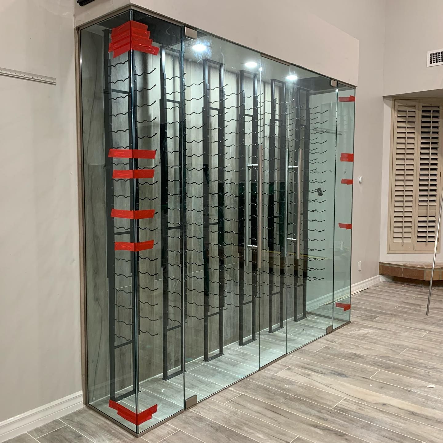 A glass wine cellar with a lot of wine bottles in it.