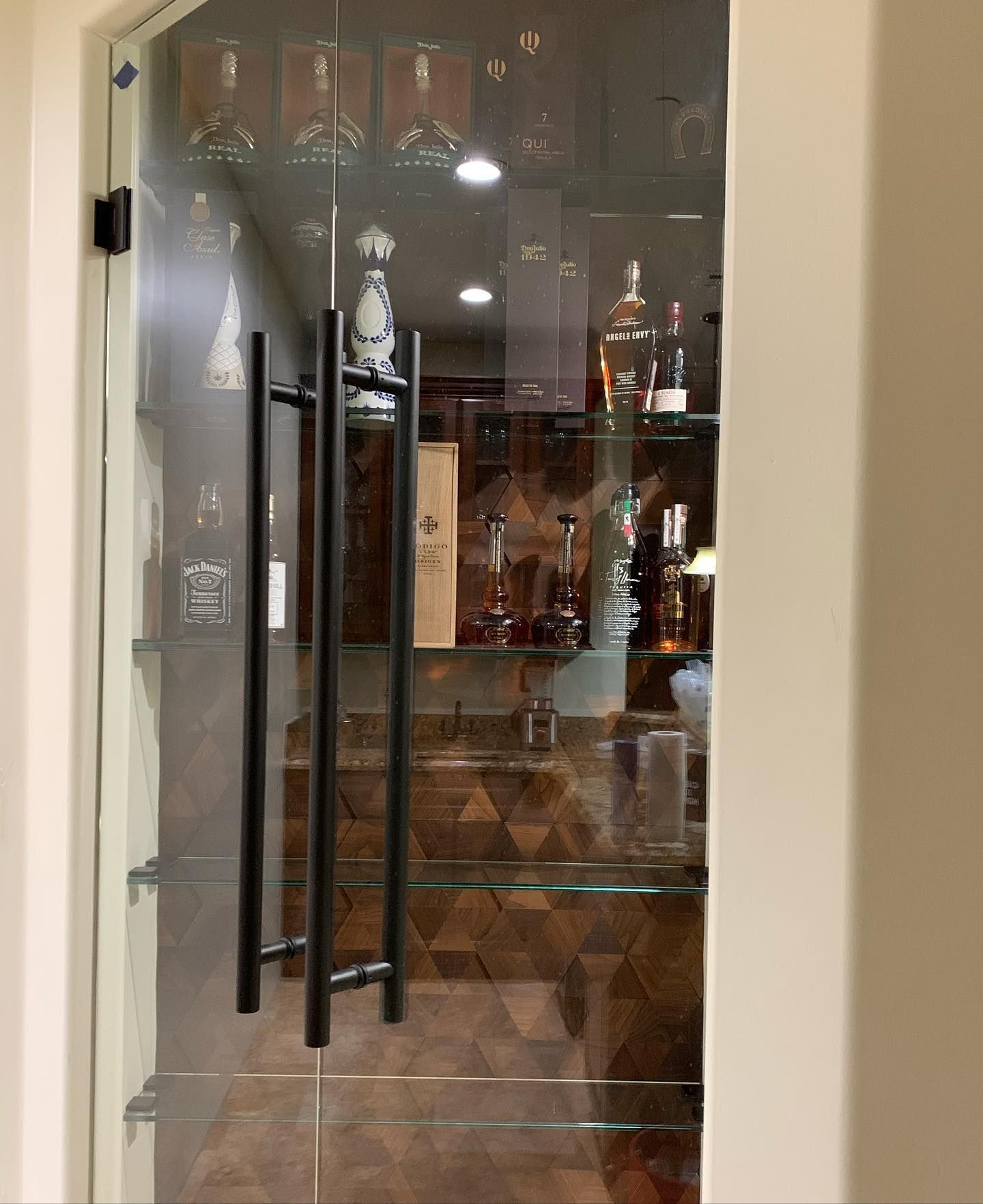 A glass door leading to a bar with bottles and glasses on shelves.