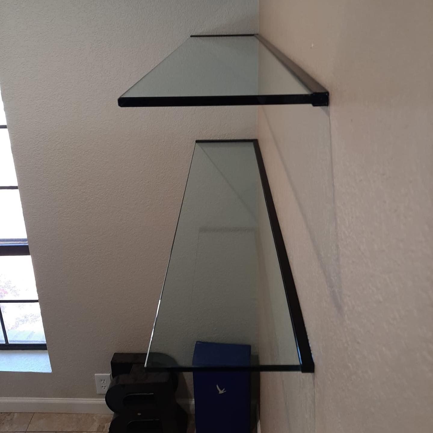 Two glass shelves are hanging on a wall next to a window