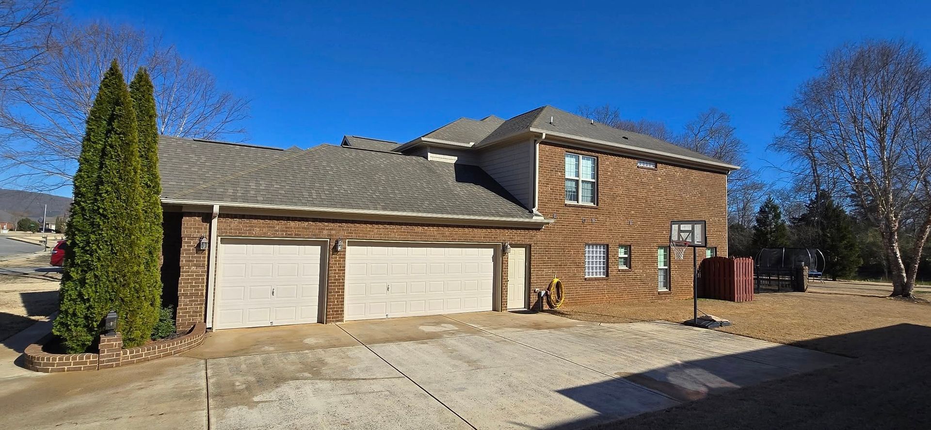 A large brick house with two garages and trees in front of it.