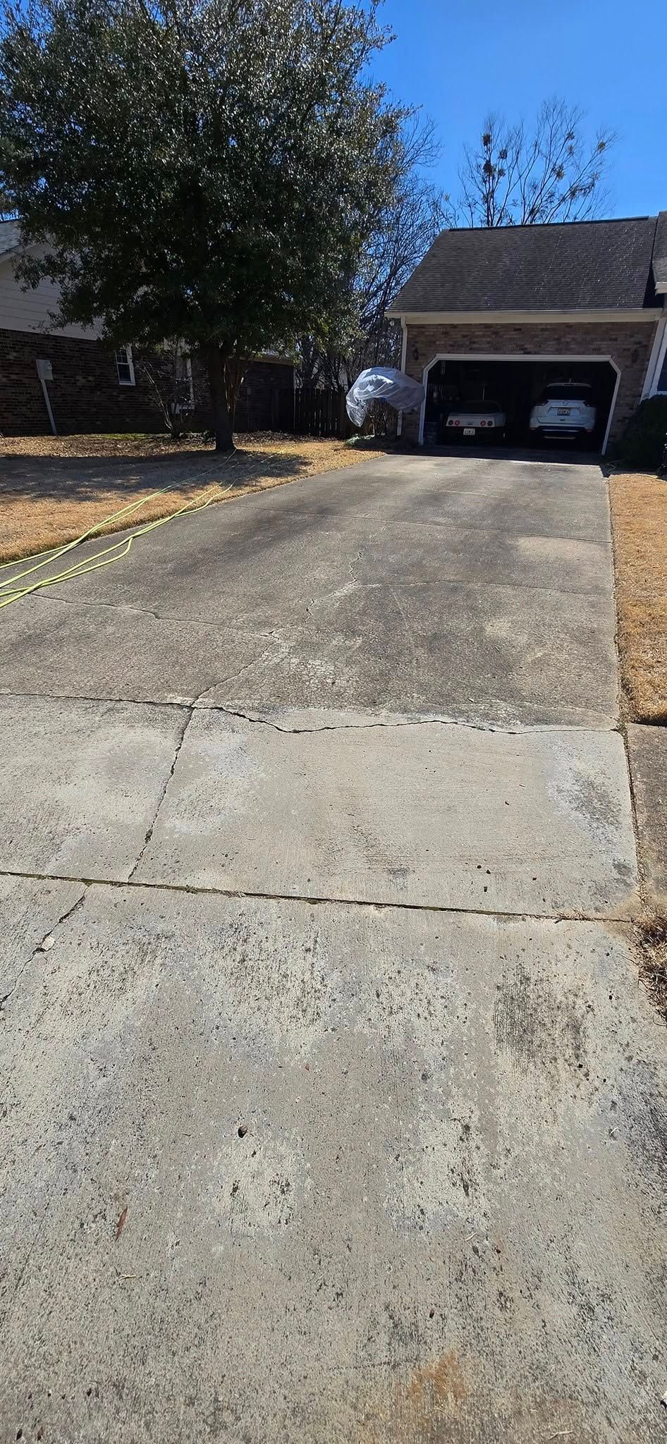 A concrete driveway leading to a house with cars parked in the garage.
