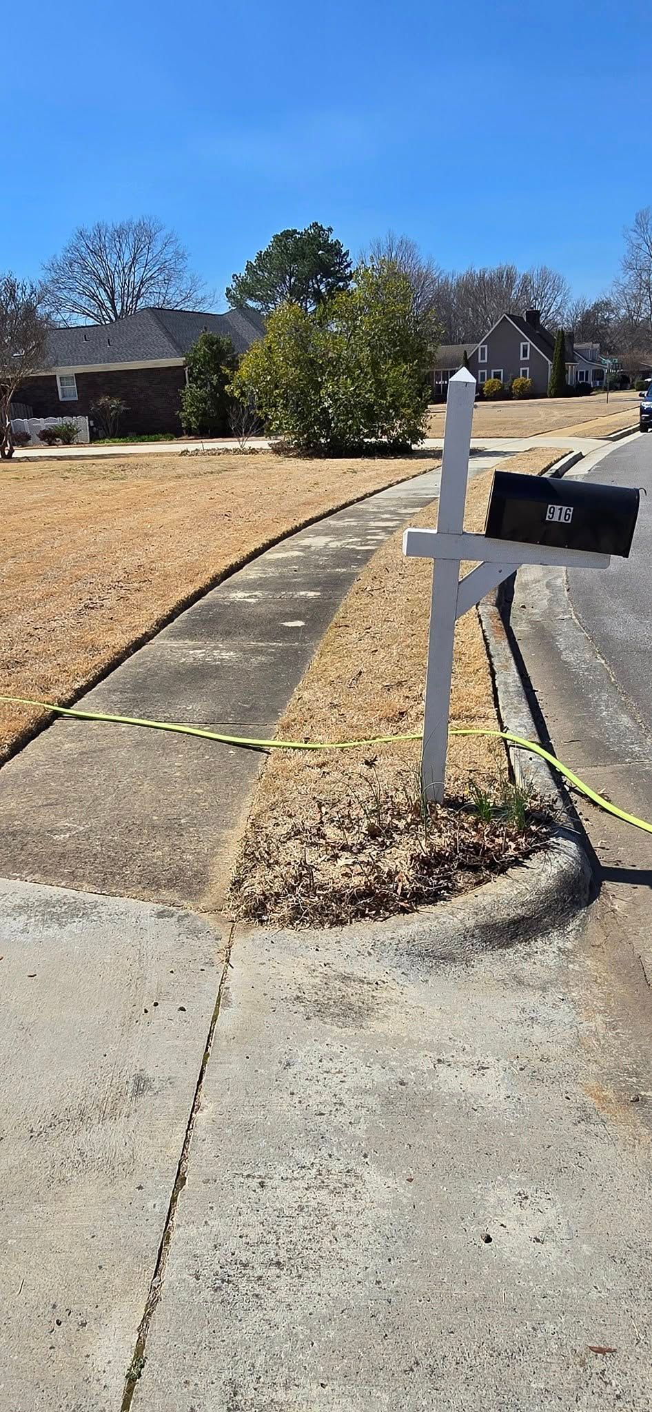 A mailbox is sitting on the side of the road next to a sidewalk.