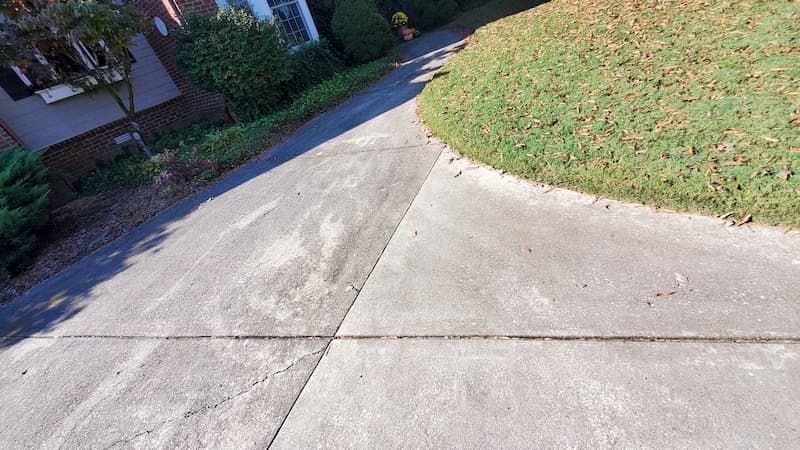 A concrete driveway with grass on the side of it and a house in the background.