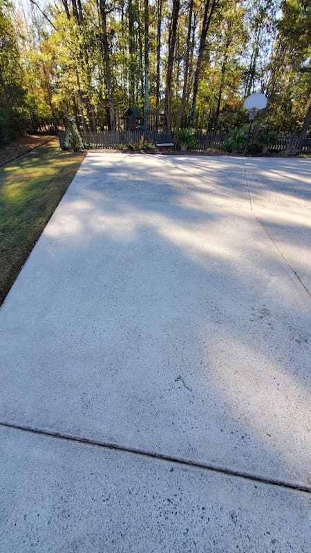 A concrete driveway leading to a house with trees in the background.