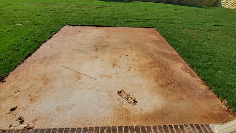 A dirty concrete driveway in a backyard next to a lush green lawn.