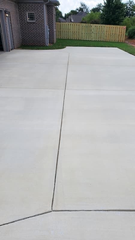 A large concrete driveway with a wooden fence in the background.
