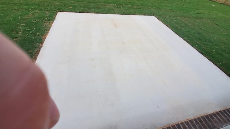 A person is standing on a concrete surface in a backyard.