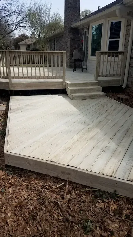 A wooden deck with stairs leading up to it is in front of a house.