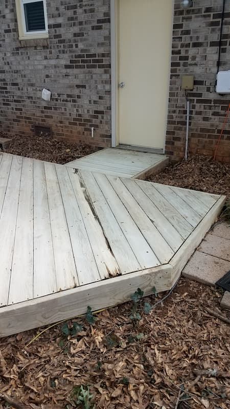 A wooden deck with a ramp leading to the door of a brick house.