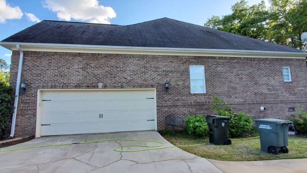 A brick house with a white garage door and two trash cans in front of it.