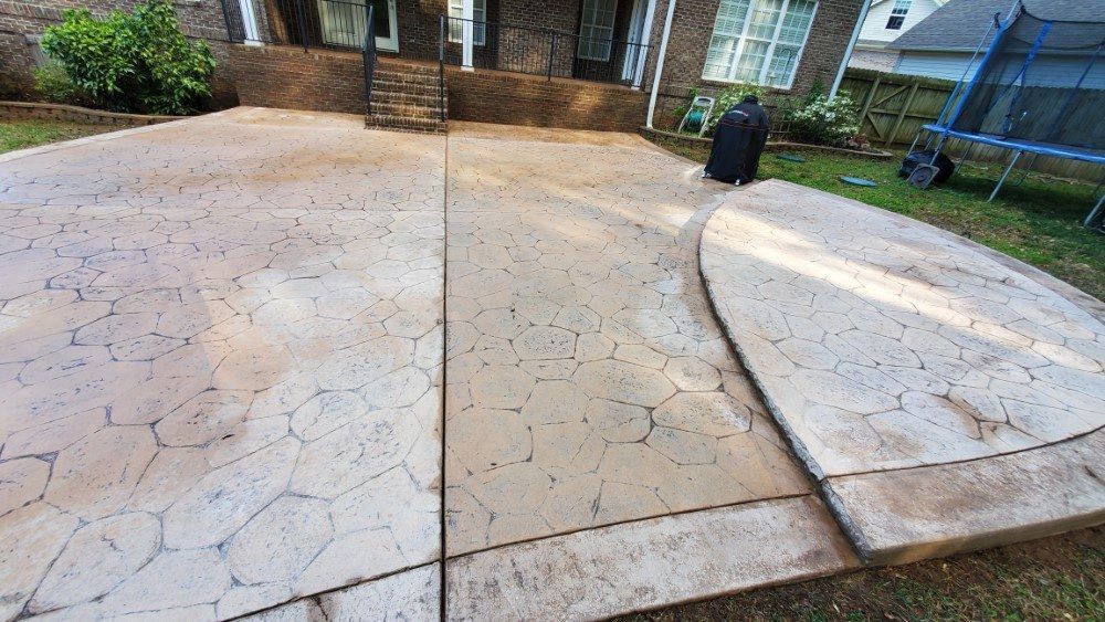 A concrete driveway in front of a house with a trampoline in the backyard.