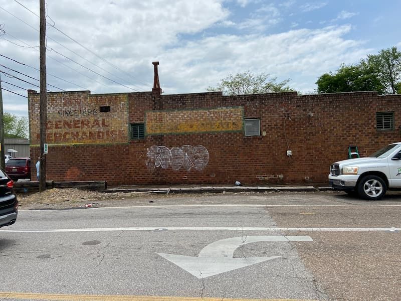 A white truck is parked in front of a brick building with graffiti on it.