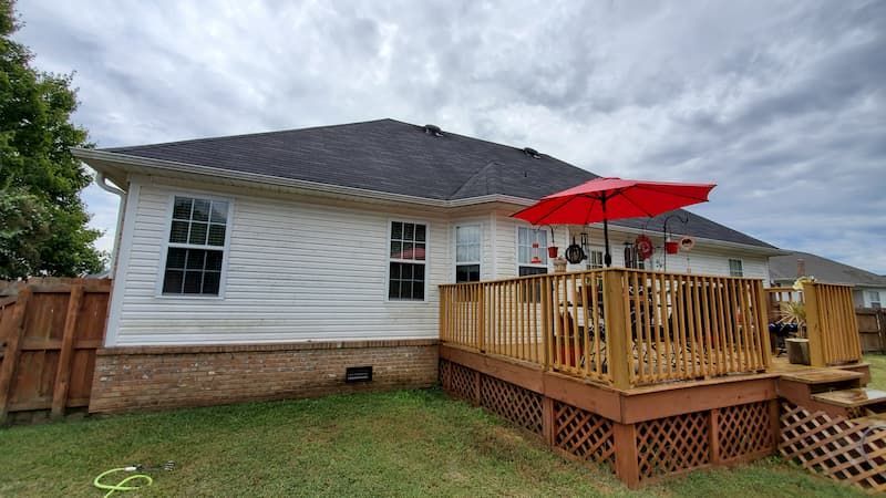 The back of a house with a wooden deck and a red umbrella.