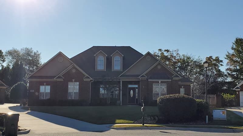 A large brick house with a black roof is sitting on top of a lush green lawn.