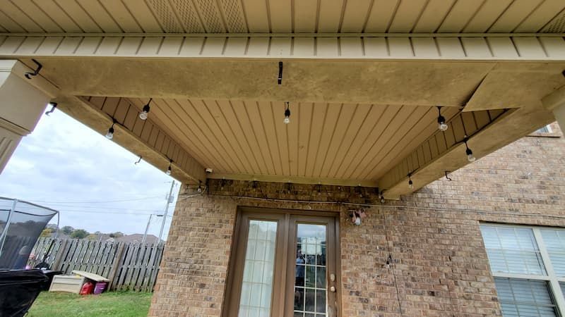 A brick house with a covered porch with lights hanging from the ceiling.