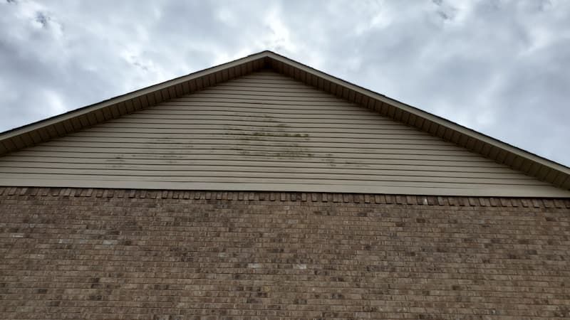 The roof of a brick house with a triangle shaped roof and a cloudy sky in the background.