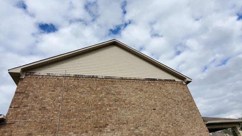 A brick house with a white roof and a blue sky in the background.
