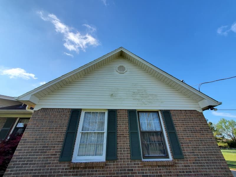 A brick house with white siding and green shutters on a sunny day.
