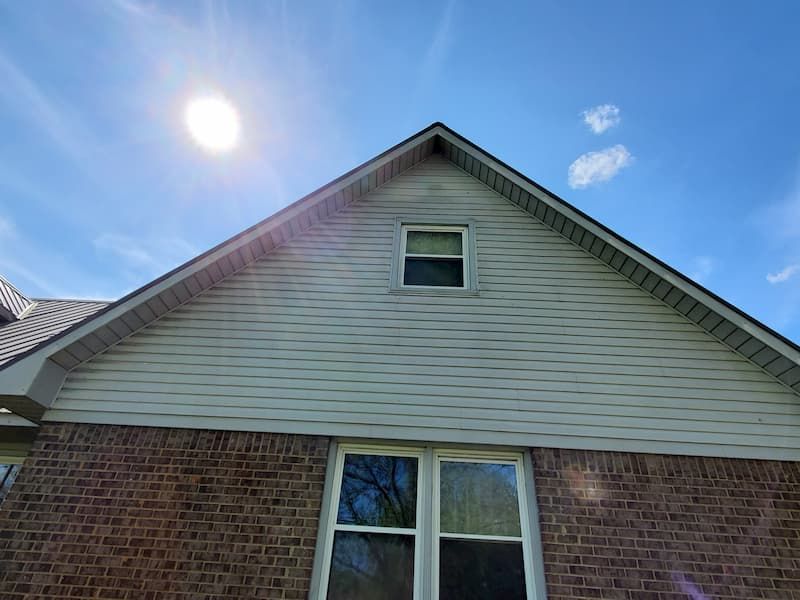 The sun is shining on the roof of a brick house with a window.