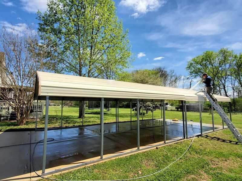 A man is standing on a ladder painting a carport.