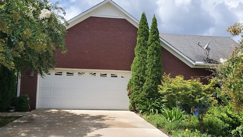 A brick house with a white garage door and a satellite dish on the roof.