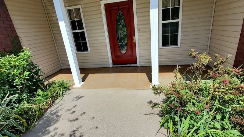 The front porch of a house with a red door and white pillars.