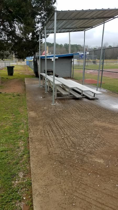 A concrete walkway leading to a baseball field with a shelter and benches.