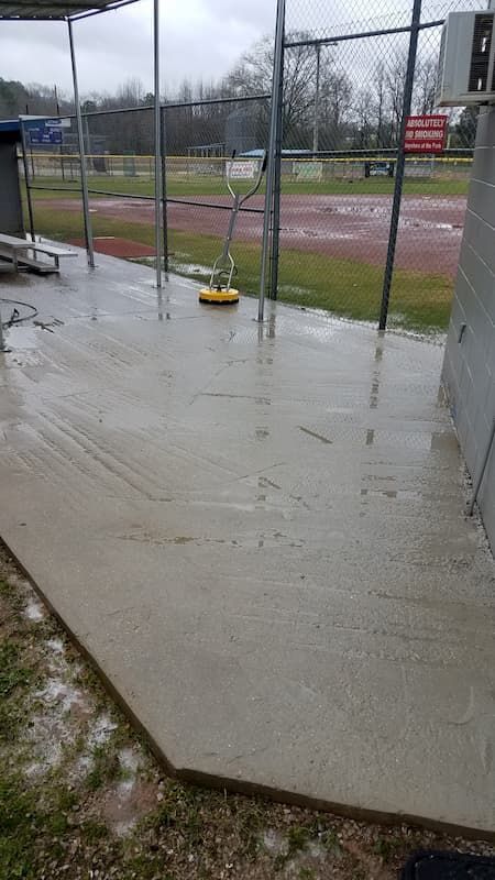 A baseball field with a concrete patio in the foreground and a fence in the background.