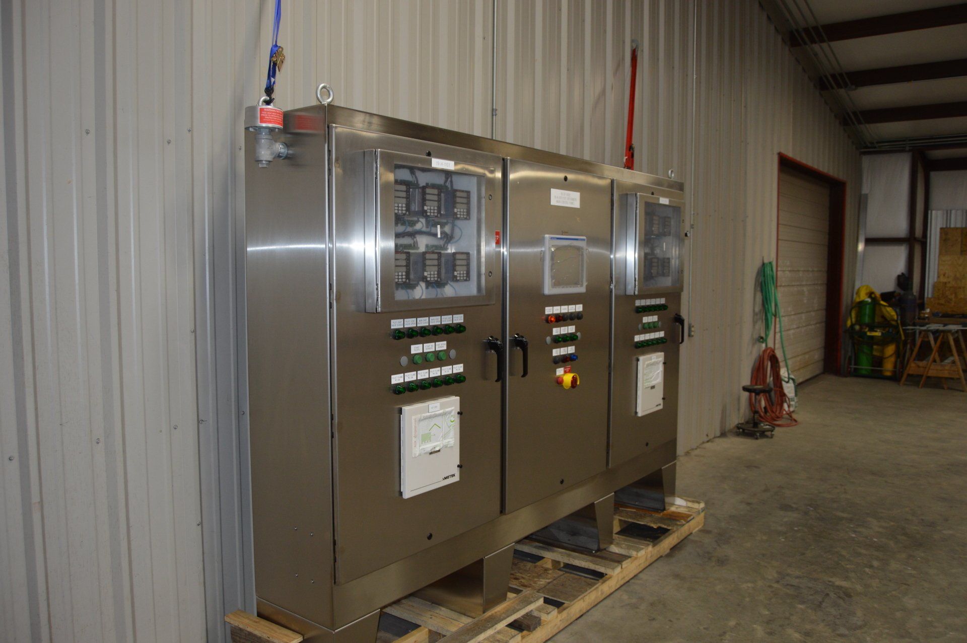 A stainless steel control panel is sitting on a wooden pallet in a warehouse.