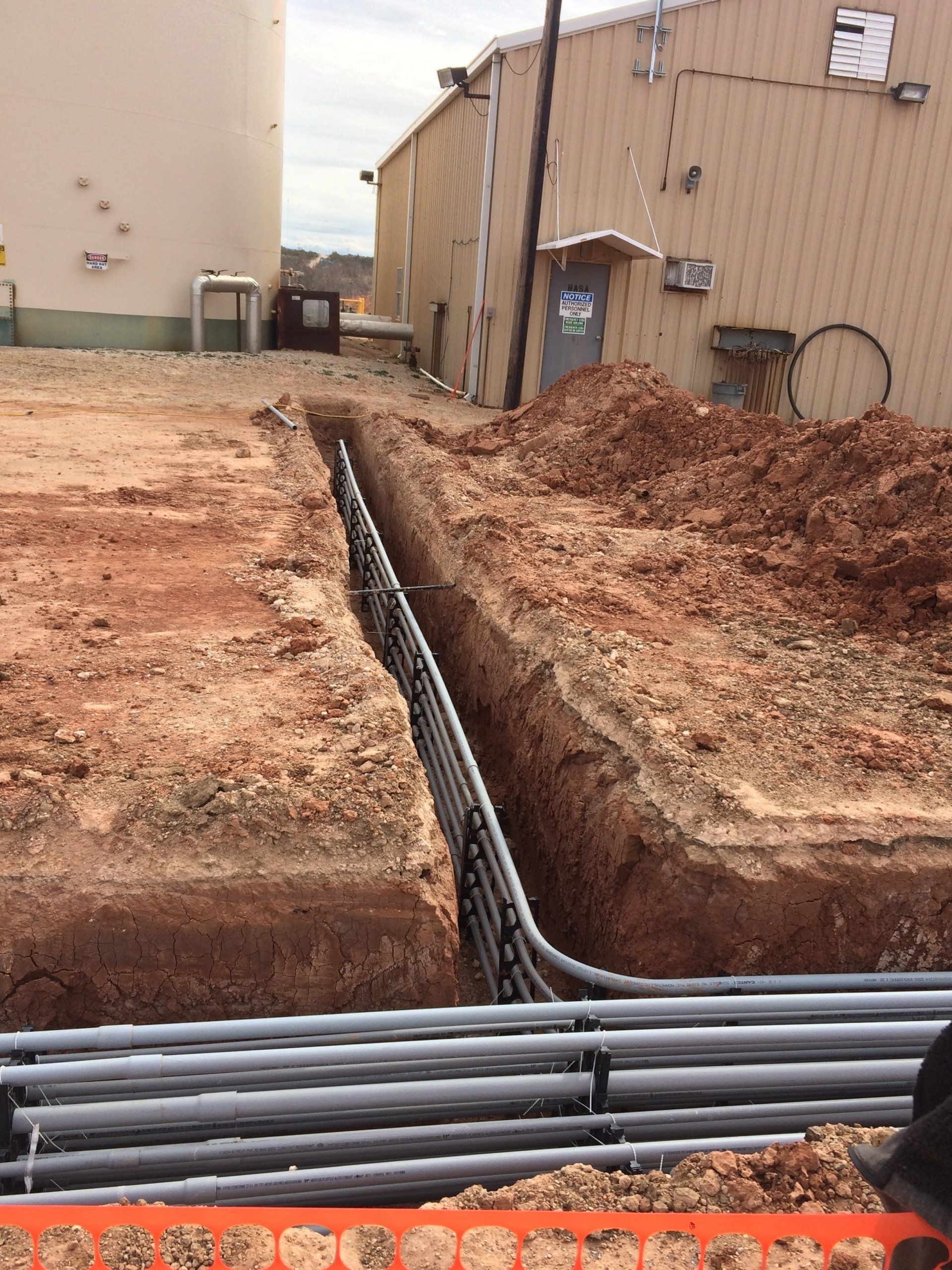 A bunch of pipes are laying in the dirt in front of a building.