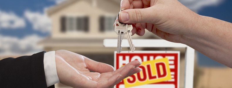 Handing over the house keys in front of real estate sign and sold new home
