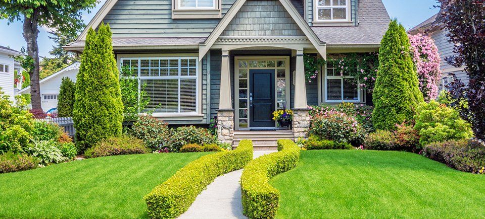Grey house with green lawn and bush-lined walkway