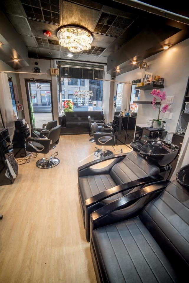 Hair salon interior with black and gray chairs, light wood floor, and decorative lighting.