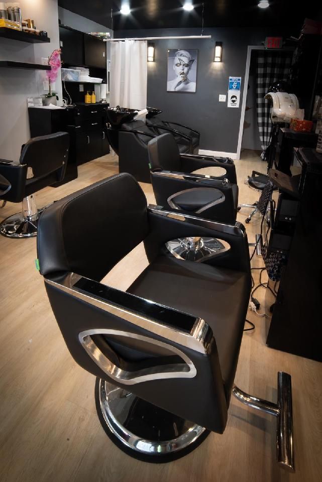 Salon with black chairs, chrome accents, and a framed portrait, with gray walls and light wood floors.