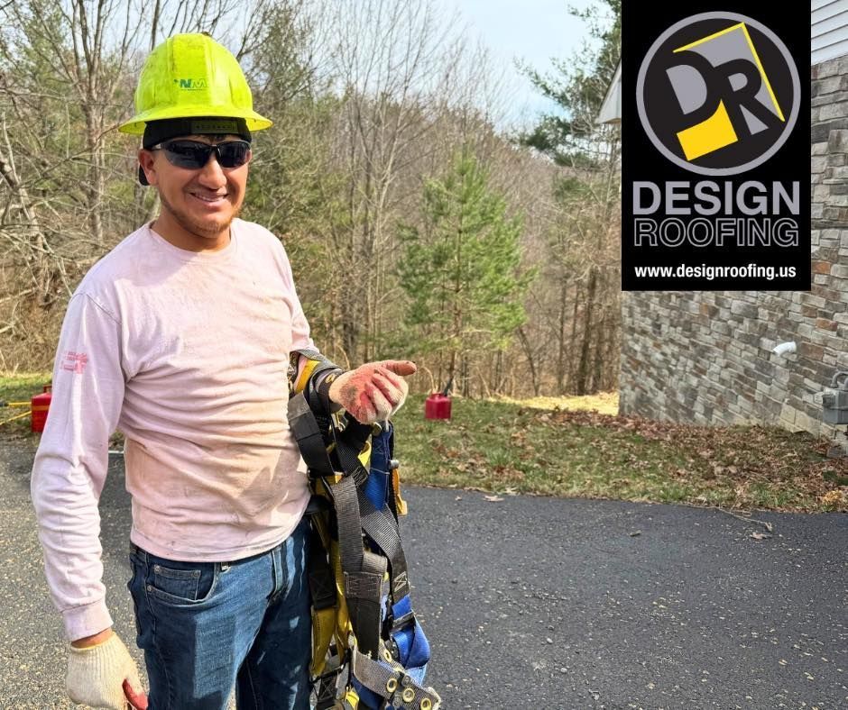 Worker in neon hard hat holding tools beside a paved driveway and DESIGN ROOFING sign.